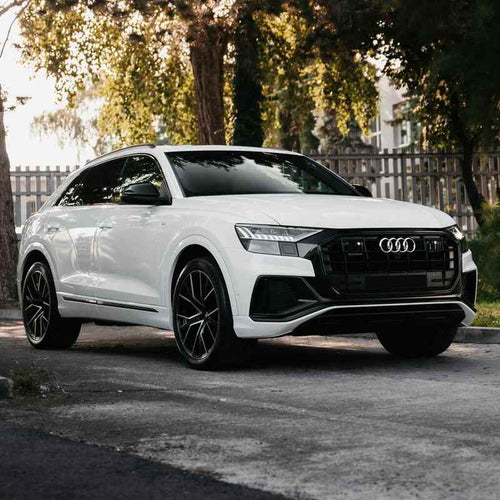 White Audi SUV parked on a street with trees in the background